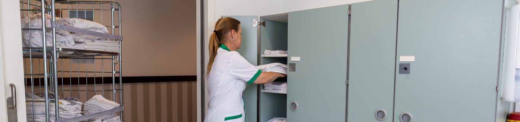 CSU schoonmaakmedewerker legt lakens in kast in een zorgomgeving
